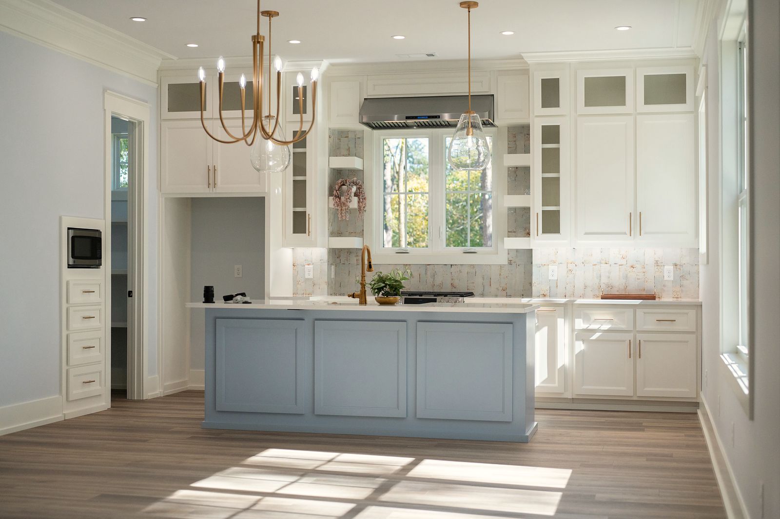 White kitchen with a blue island and brass pendant lights, East Alabama